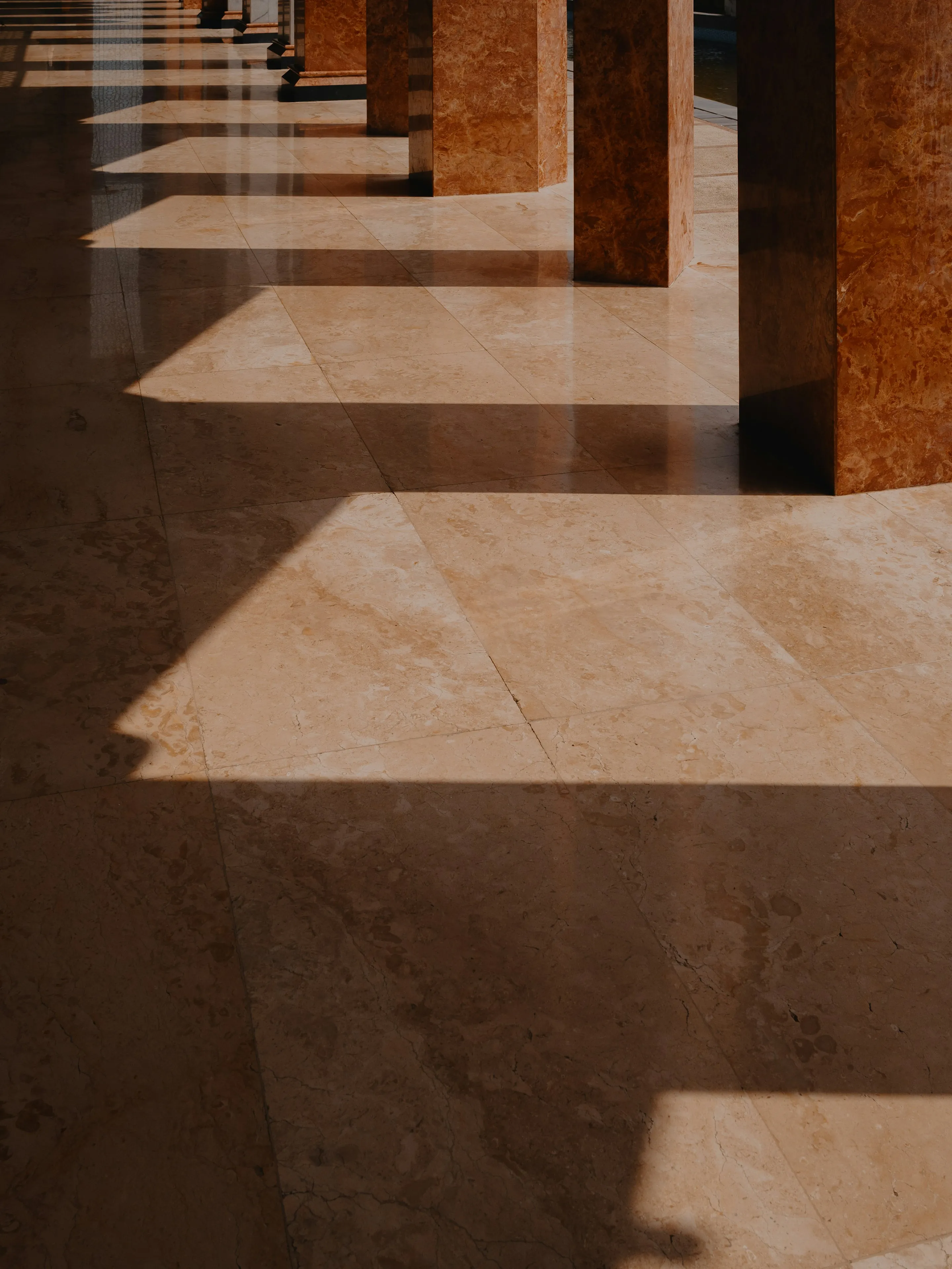 Sol en marbre poli et lustré, traversé par le soleil qui dessine l’ombre des colonnes.