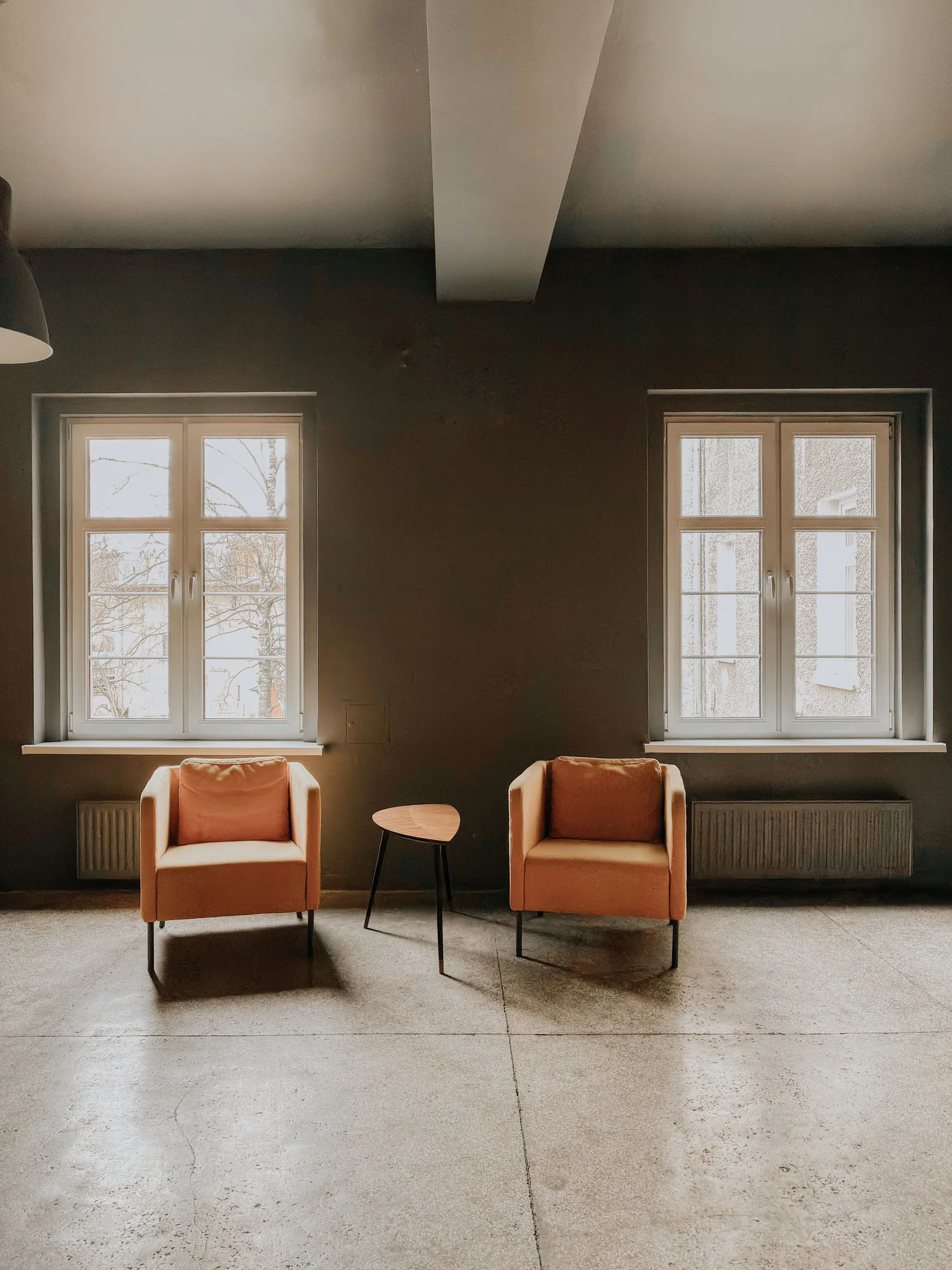 Deux fauteuils orange et une petite table dans une pièce calme, baignée par la lumière de deux grandes fenêtres.