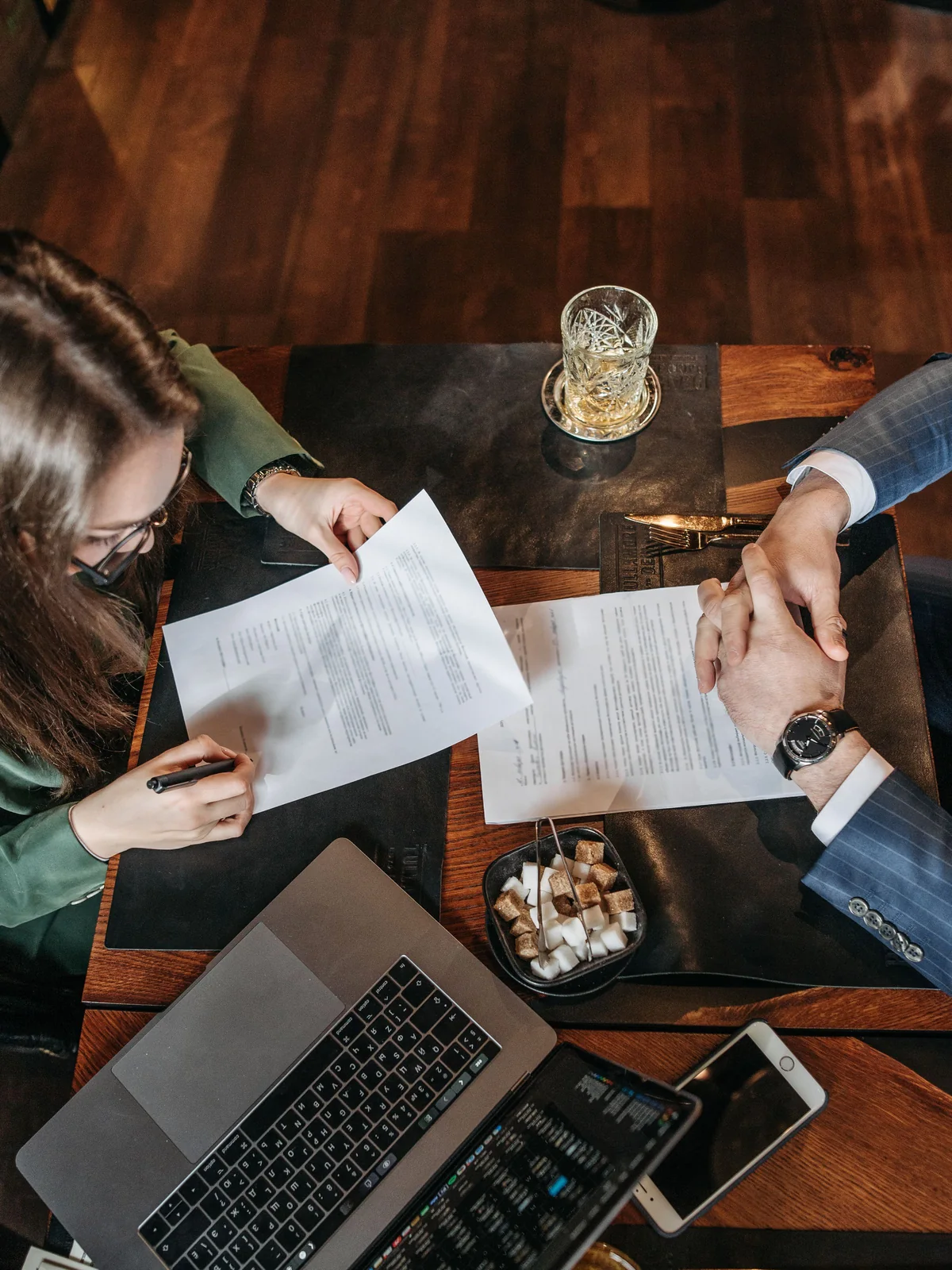 Vue de dessus d’une table où deux personnes échangent les pages d’un contrat, stylo en main, une signature déjà portée sur le document de droite.